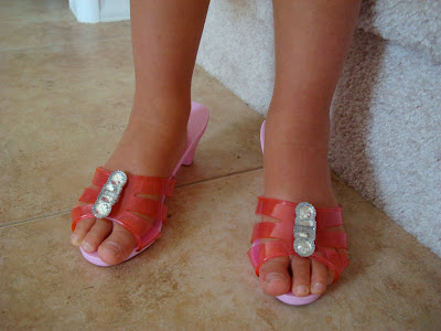 Feet in child high heels showing the pink strapy color