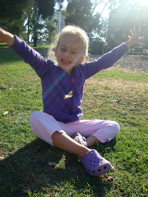 Young girl sitting in grass with arms up in the air