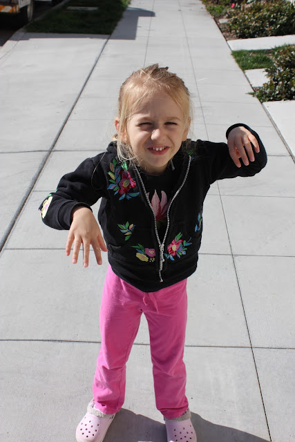 Young girl with arms half raised smiling on sidewalk