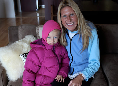 Young girl in puffer jacket sitting on couch with woman in blue vest