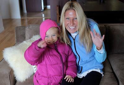 Young girl in jacket and woman in vest on couch waving