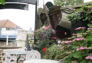Pub tables and chairs with half a boat sticking out of a wall in the garden