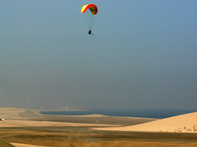 A paraglider hangs high above the desert