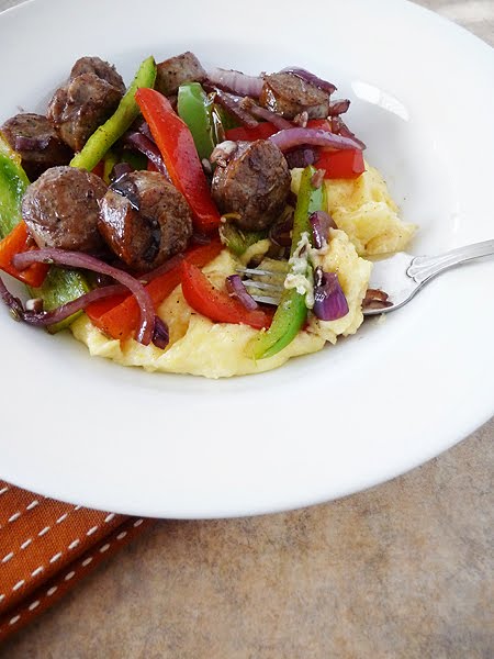 A white bowl of mascarpone polenta topped with sausage and peppers. 