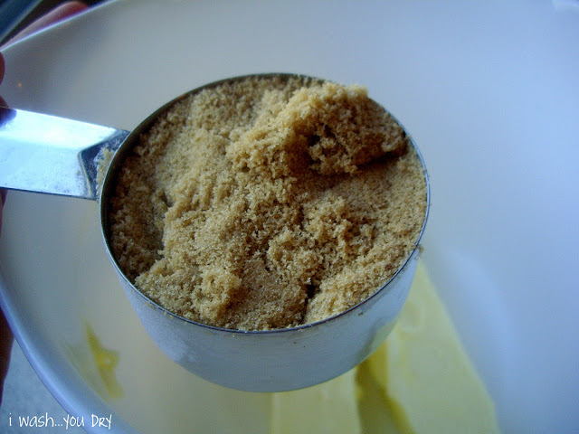 A measuring cup of brown sugar above a bowl with two sticks of butter in it. 
