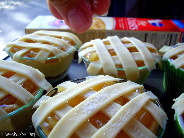A hand sprinkling sugar on top of mini pies before they are baked. . 