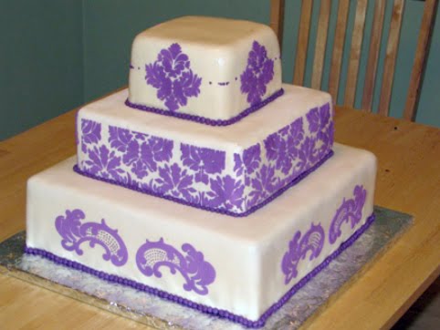 Three tier square white wedding cake with purple damask pattern