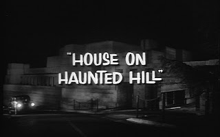 Em preto e branco, uma imagem externa da residência robusta em estilo moderno e o entorno escuro (noite), com um carro subindo por uma pista margeando a casa com os faróis acesos. Em primeiro plano, escrito em branco no centro da tela, o nome do filme: "House on Haunted Hill".