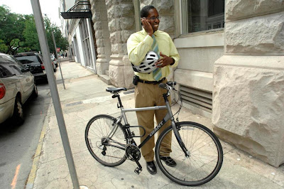 Image of bicyclist taking a cell phone call, standing on the sidewalk next to his bike