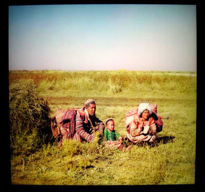 Nomadic man, woman and child sit in a field with their belongings