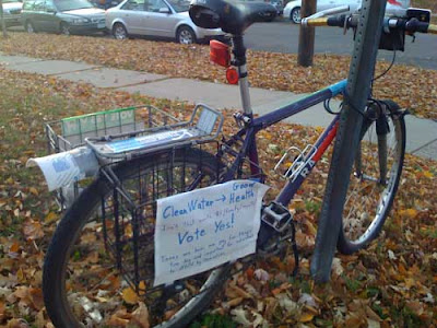 Photo of a bicycle hung with several environmentally oriented signs, and with half a yogurt container taped on to keep mud from splashing up the back of the bike