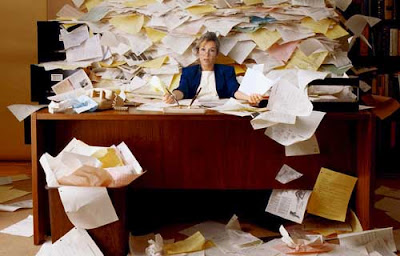 Photo of a woman at a desk almost buried in office paper