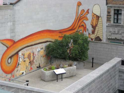 Large graffiti-like painting of a serpent in orange, over a small concrete planter with brown grasses visible