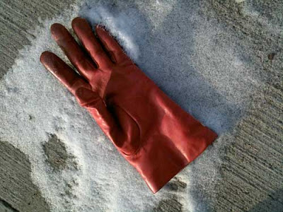 A single red leather glove lying in a patch of white snow on a sidewalk