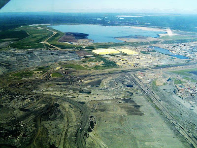 Aerial shot of a large strip mine and tailings ponds surrounded by green tracts of forest
