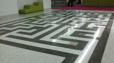Black and white maze in a shiny floor with a green modernist couch in the background