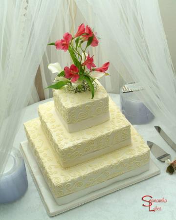 Three tier square wedding cake with swirls and flowers on top