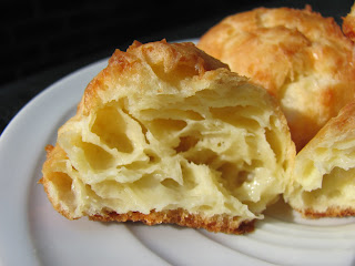 Gougères AKA French Cheese Puffs on a white plate with one broken open to see the inside texture