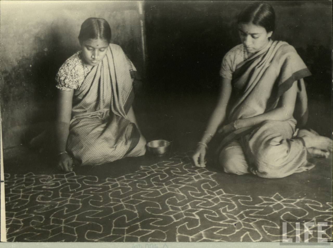 Two ladies creating Alpana (Rangoli) on the floor