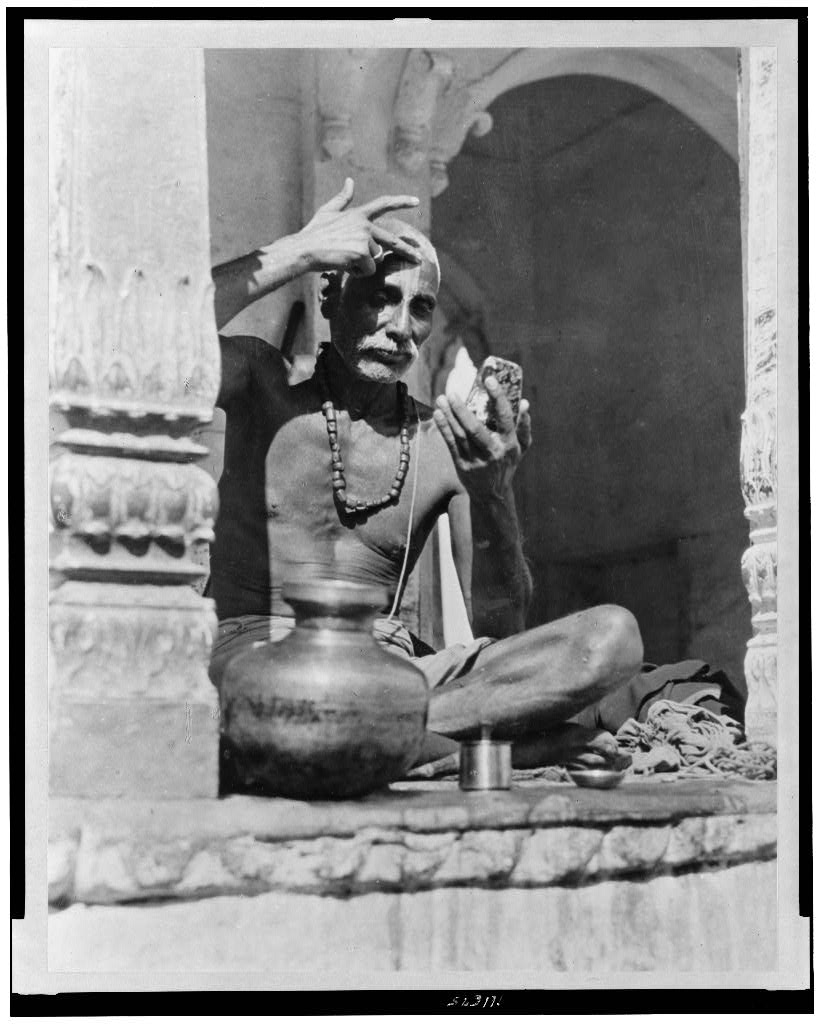 Brahman priest painting his forehead with the red and white marks of his sect and caste - Early 20th Century