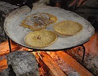 A color photo of tortillas cooking on an iron comal.