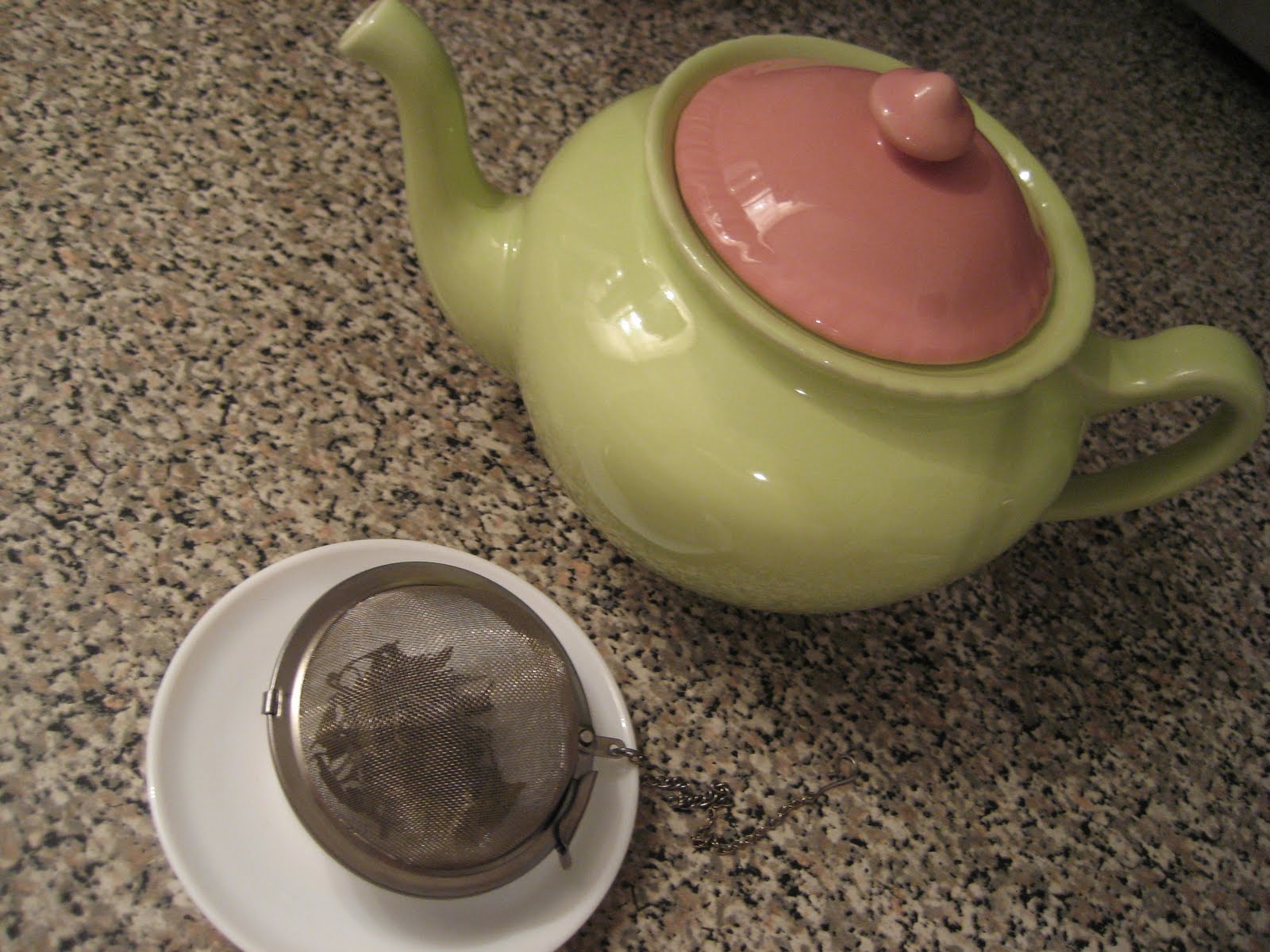 A close-up of hands pouring hot water over linden blossoms in a glass teapot, with steam rising and a timer app open on a smartphone nearby