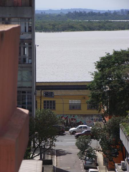 foto do blog Vivendo Porto Alegre apresentando A Avenida Mauá, o Muro do Cais do Porto, o Cais Mauá, o Guaíba e alguns de seus arquipélagos em um dia parcialmente nublado na cidade. Imagem obtida da Casa de Cultura Mário Quintana
