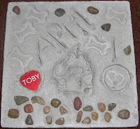 Picture of Toby's pawprint stone. Which has his pawprint in it, and also his dog tag.