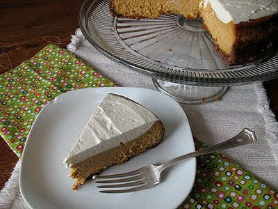 A slice of pumpkin cheesecake with rum whipped topping resting on a plate with the whole cheesecake in the background. 