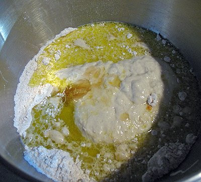 An overhead photo of poolish, flour, salt, yeast, cinnamon, nutmeg, allspice, cloves, orange extract, eggs, honey, oil and warmed milk in a bowl. 