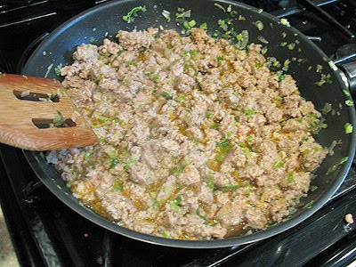A close up photo of cooked sausage, shallots, and garlic in a large saute pan.
