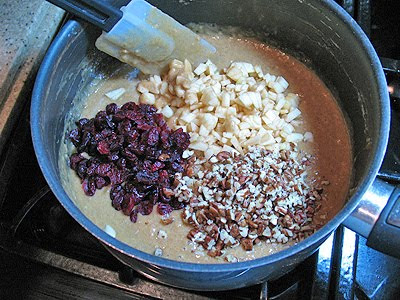 A close up photo of chopped apple, raisins and nuts being mixed into the batter.
