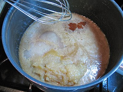 A close up photo of applesauce, vanilla and rum being whisked into the butter and brown sugar mixture.